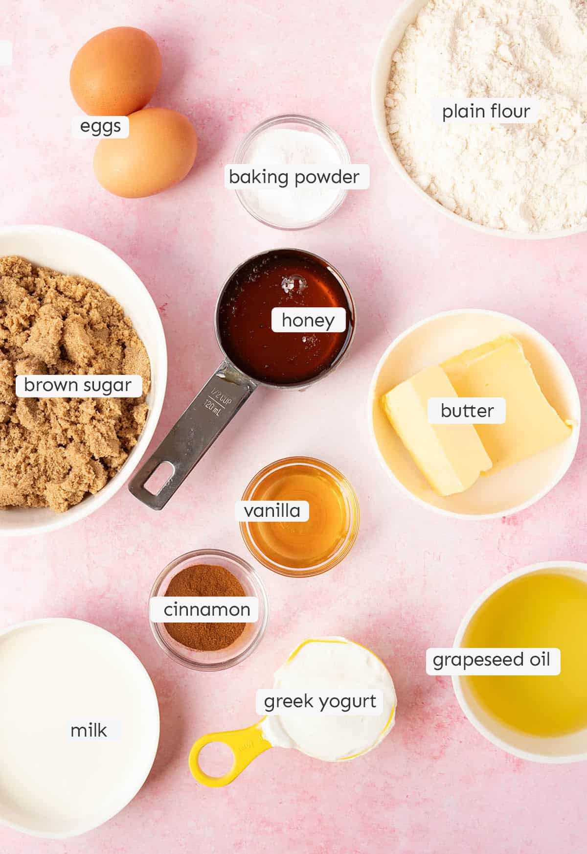 All the ingredients to make a Honey Cake from scratch laid out on a pink backdrop. 