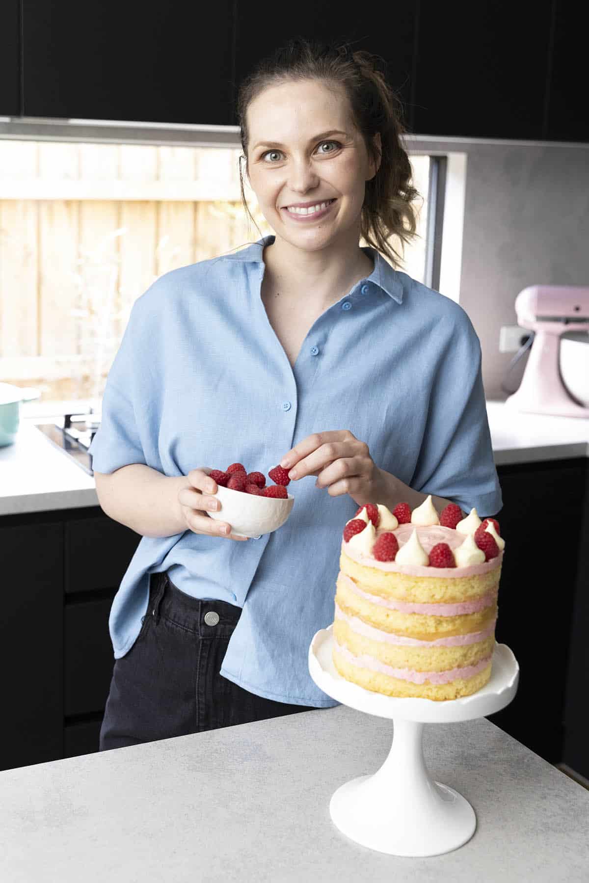 Jessica Holmes decorating a layer cake in her kitchen.