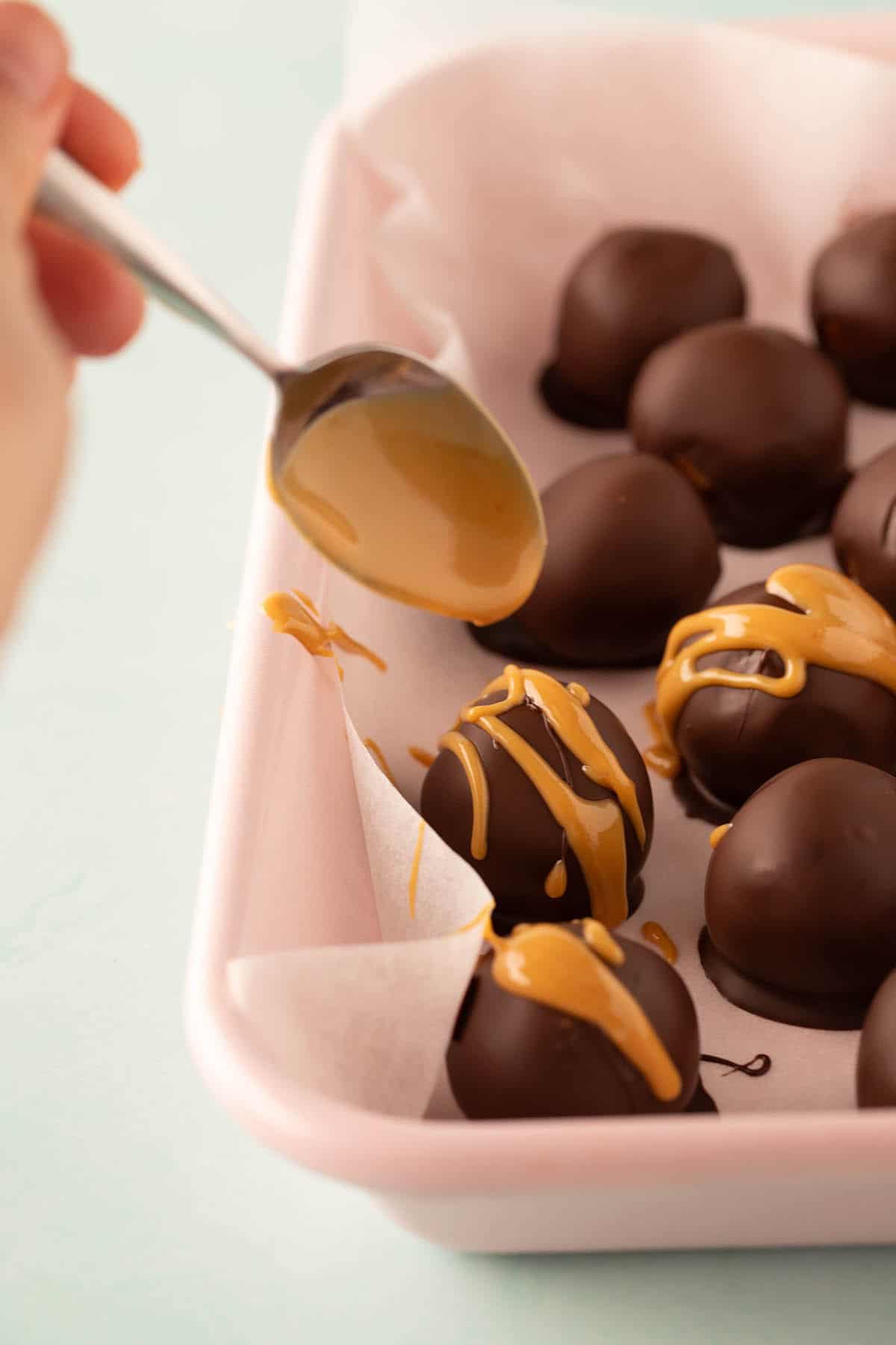A tray of homemade peanut butter balls being drizzled with peanut butter. 