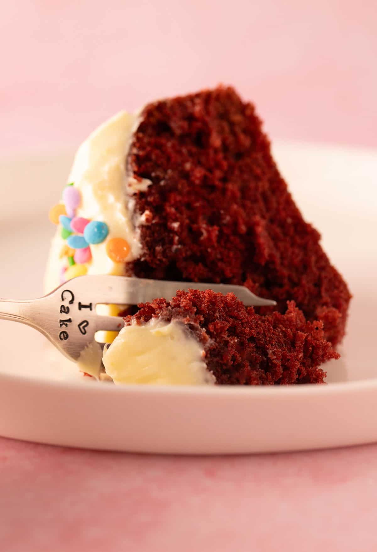 A decorative fork diving into a small piece of Red Velvet Cake.