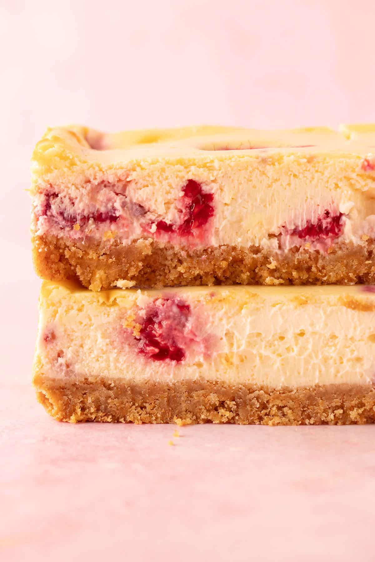 Close up of a stack of white chocolate cheesecake bars with gooey raspberries.