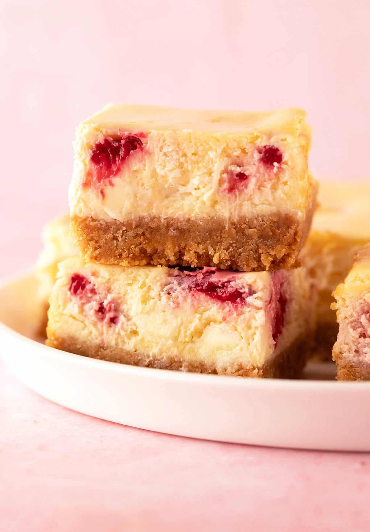 A stack of homemade white chocolate raspberry cheesecake bars on a white plate.