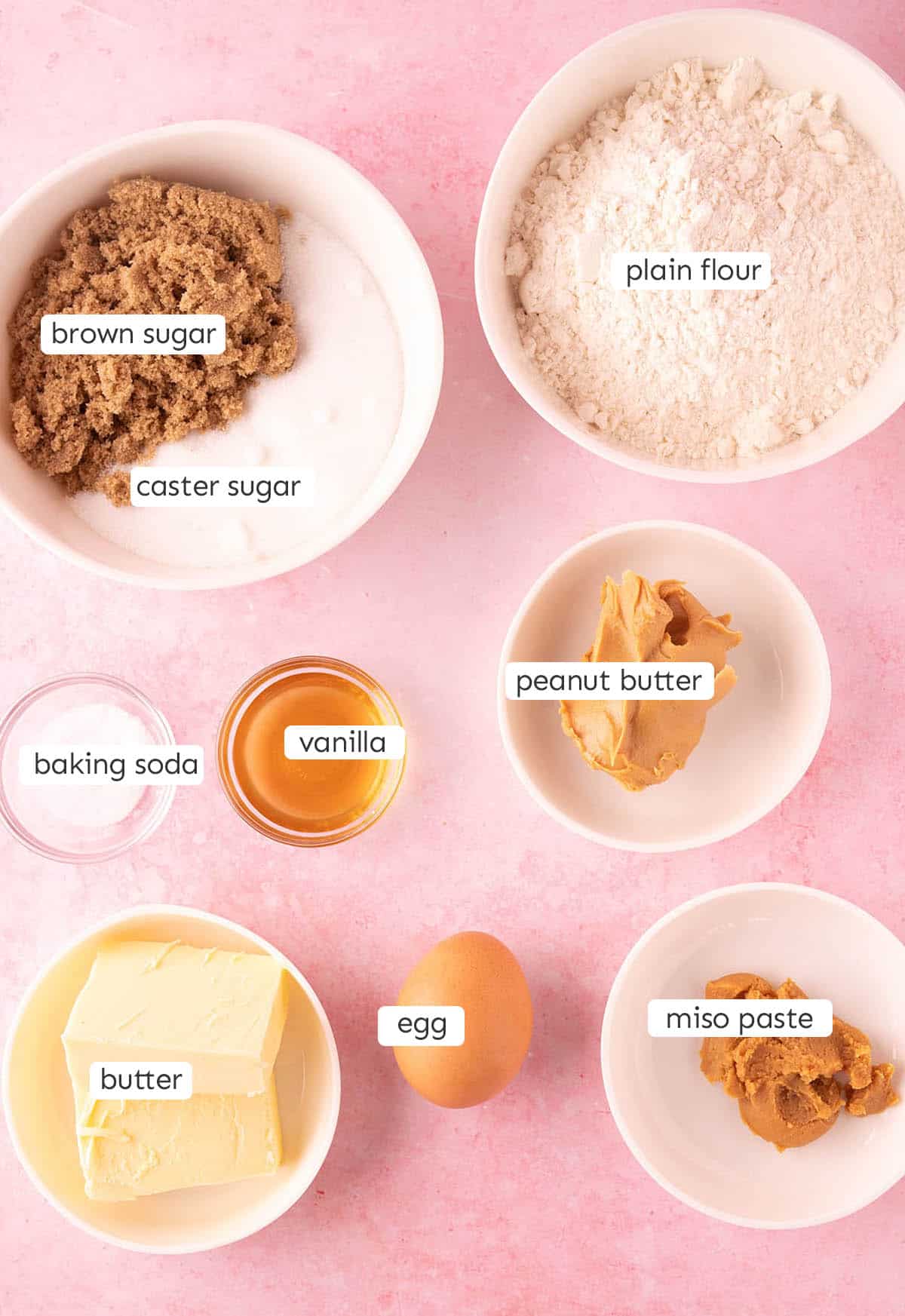 All the ingredients needed to make Peanut Butter Miso Cookies from scratch on a pink background.