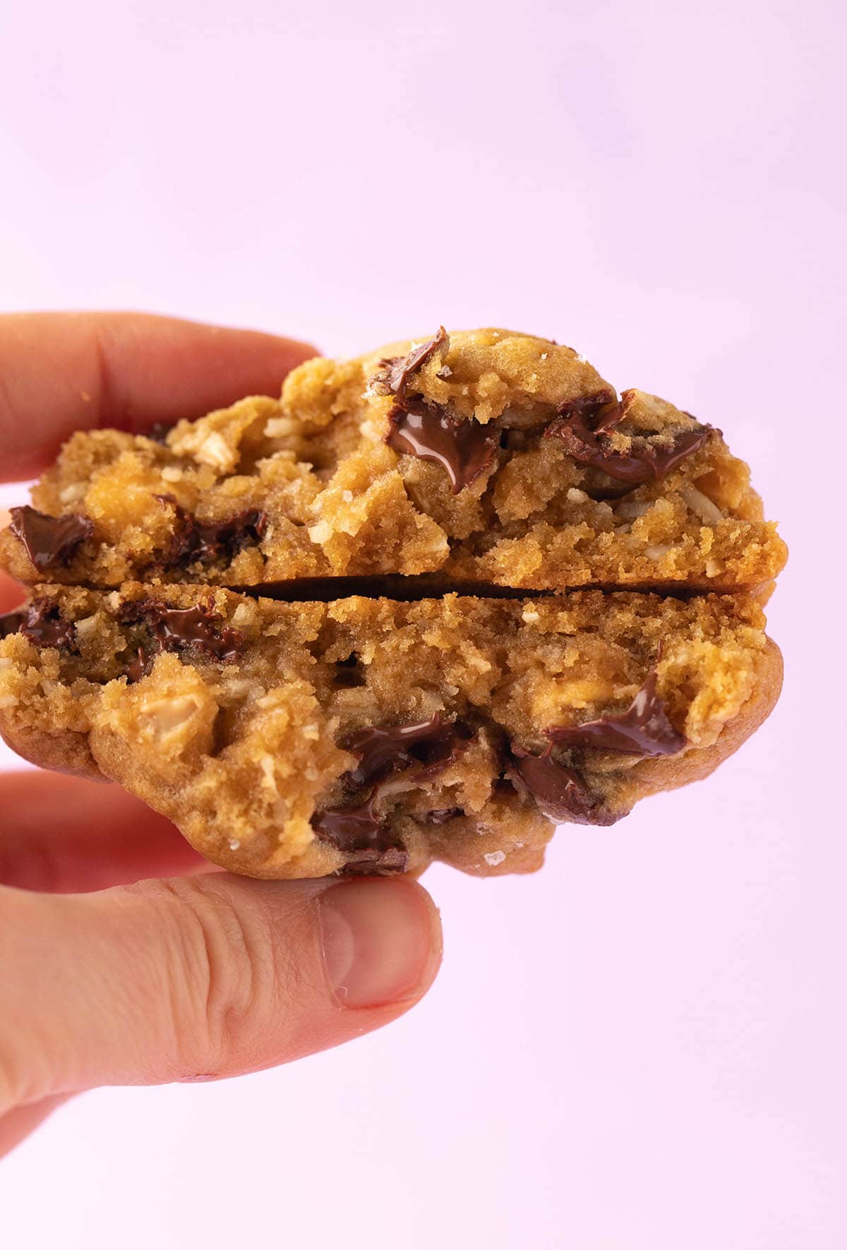 A hand holding a Caramel Coconut Cookie with gooey chocolate chips. 