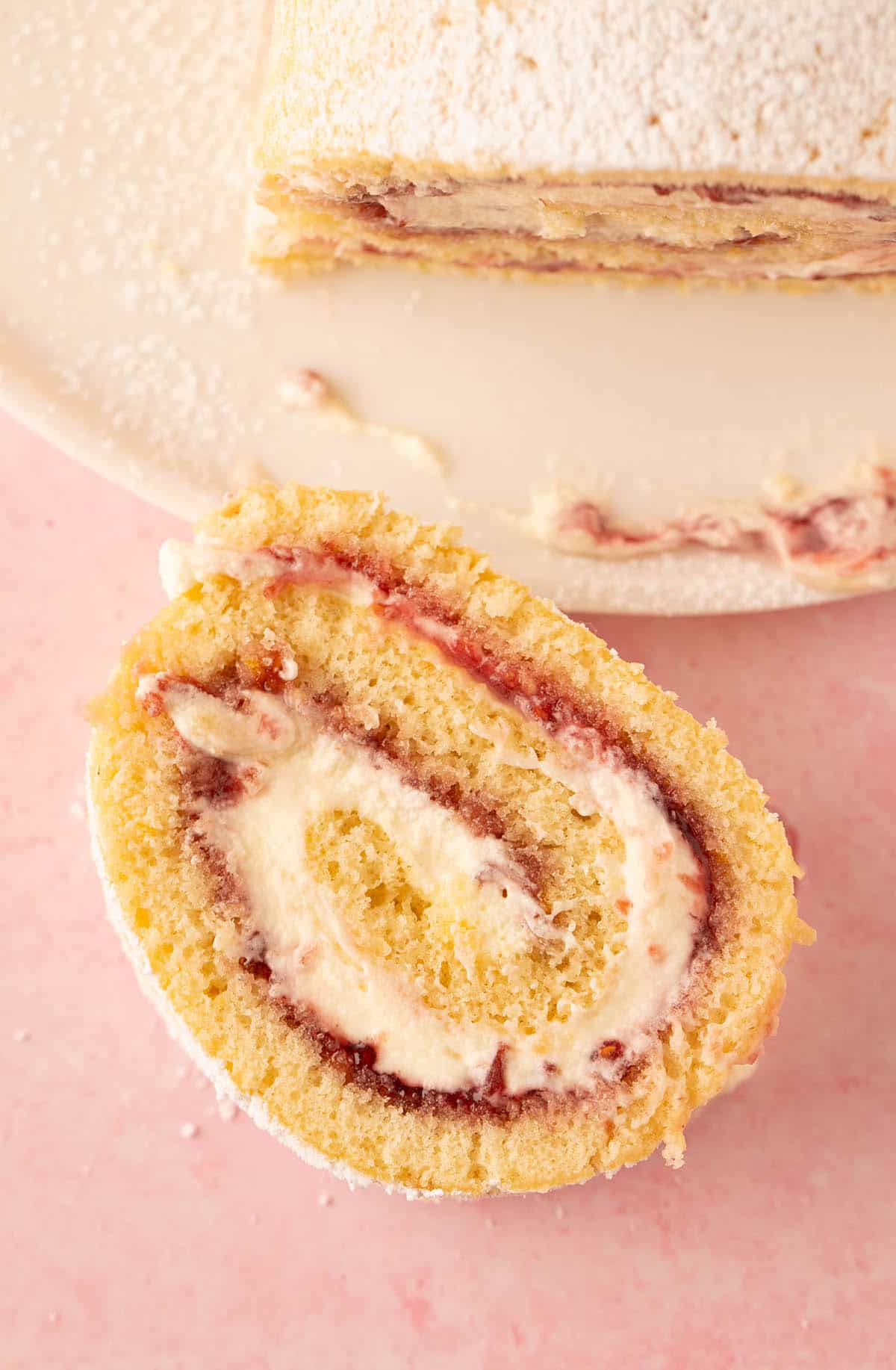 A beautiful slice of vanilla cake roll on a pink backdrop.