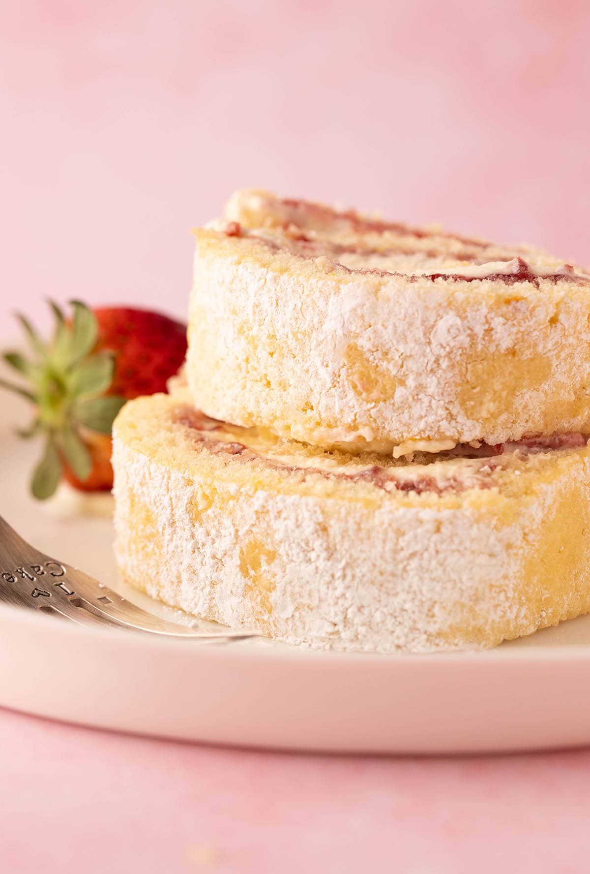 A stack of swiss cake roll slices served with fresh strawberries.