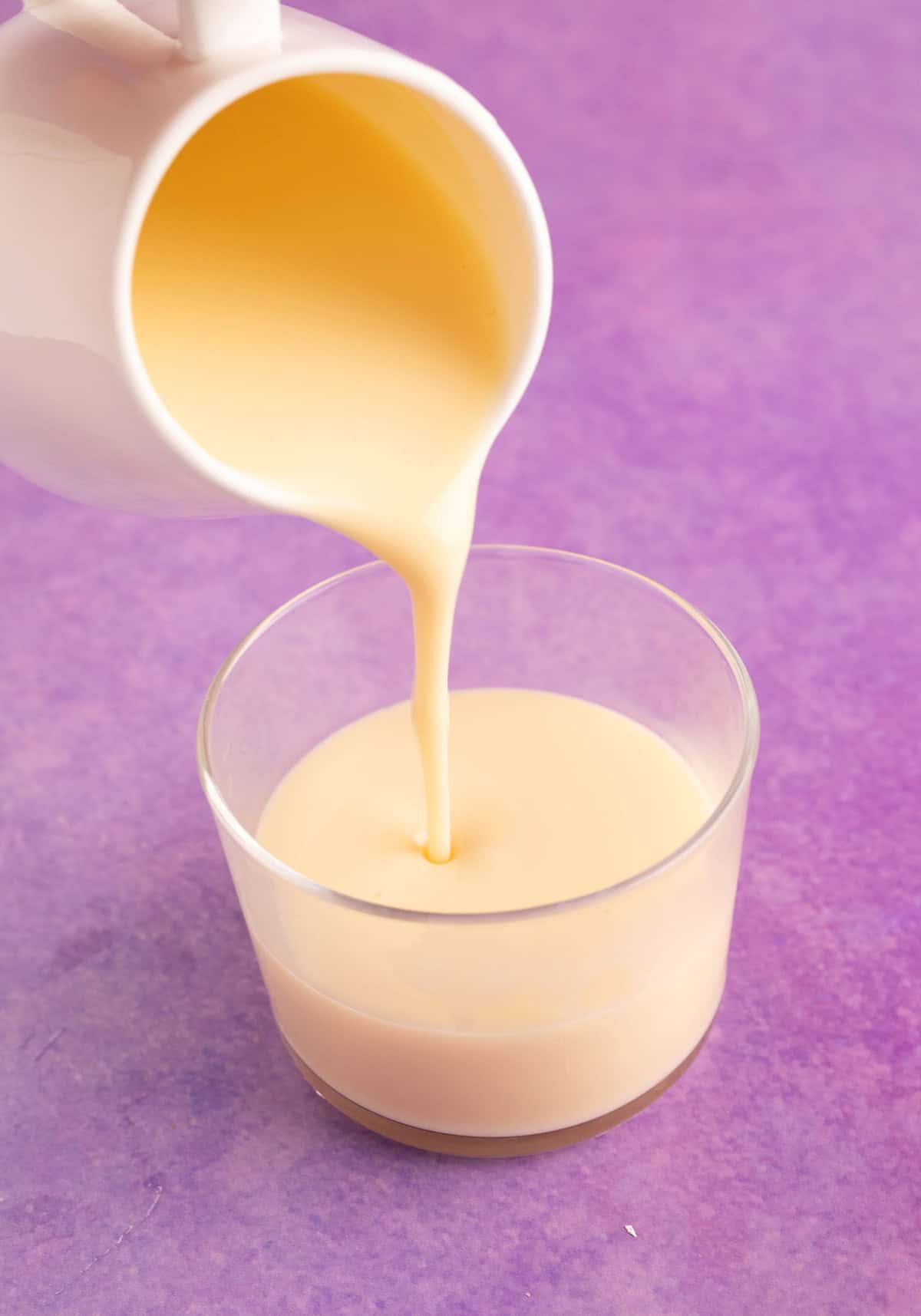 Pouring custard in a glass jar on a purple backdrop.