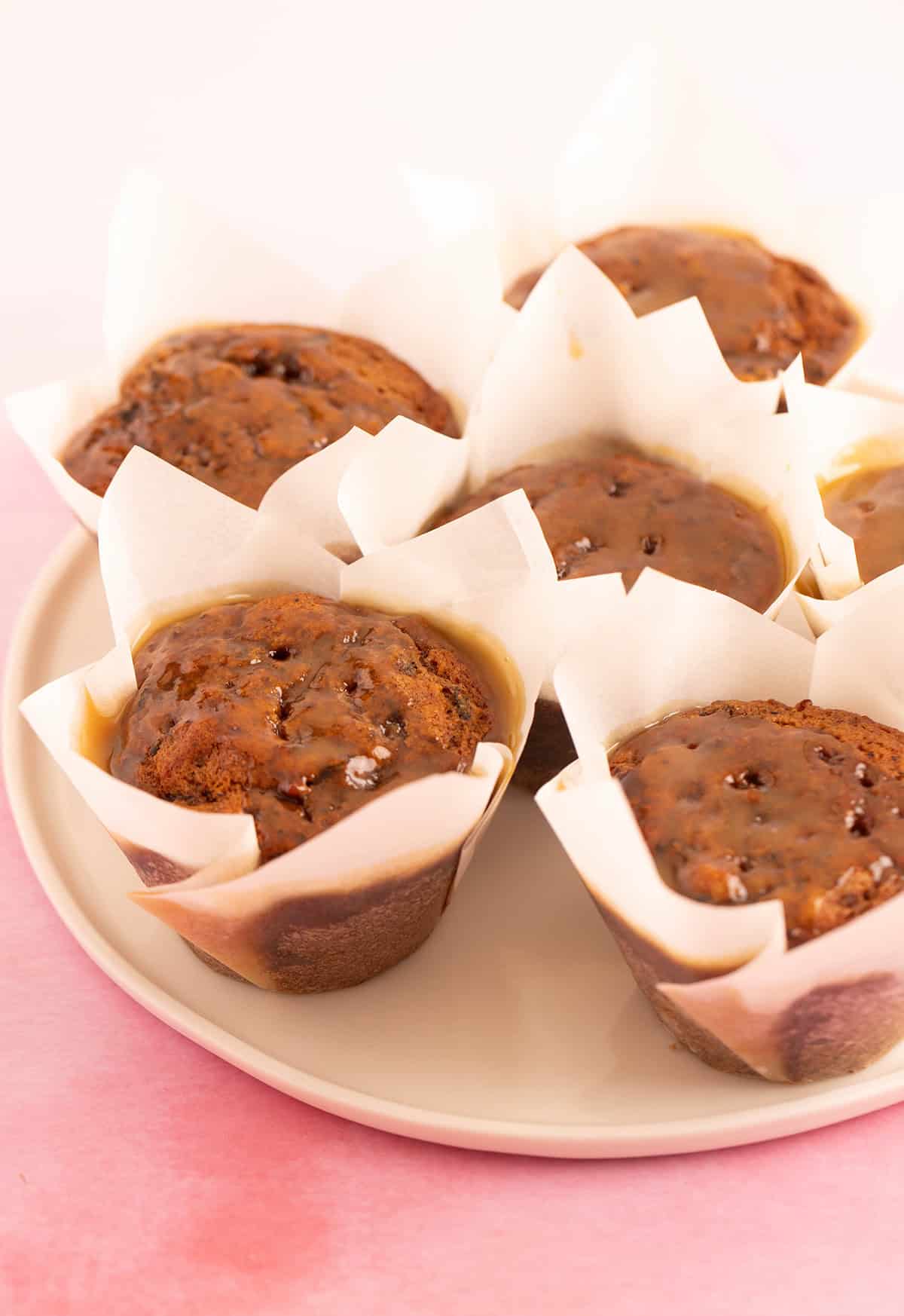 A plate of gooey Sticky Date Puddings on a pink backdrops. 