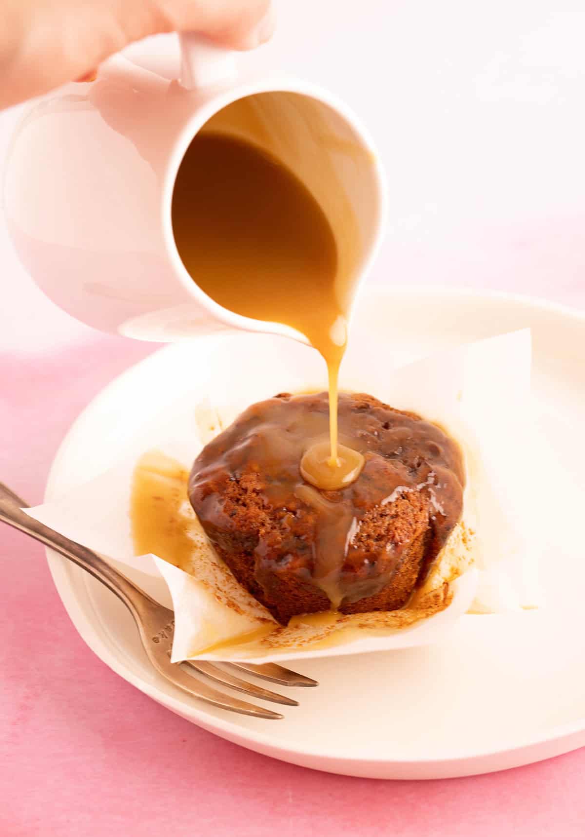 A sticky date muffin on a plate with gooey caramel sauce being poured over the top. 