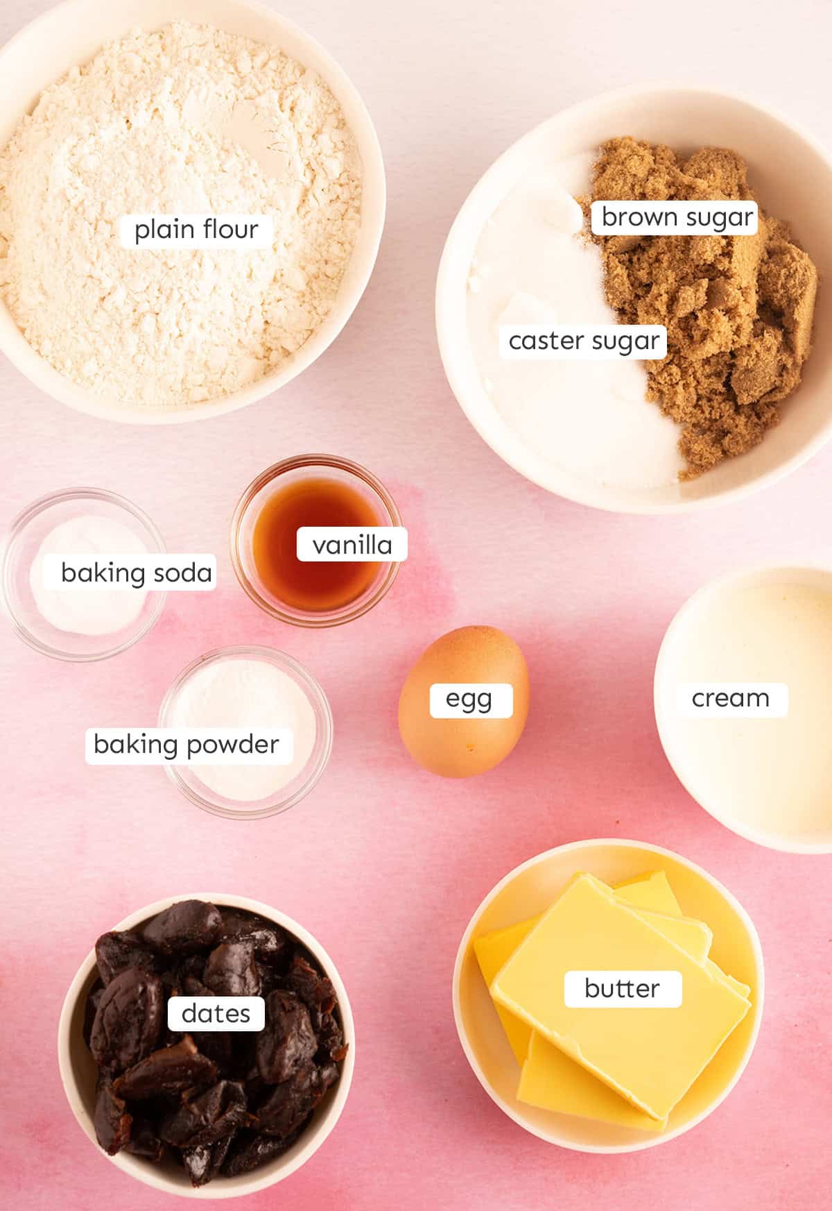 All the ingredients needed to make Sticky Date Pudding from scratch on a pink background. 
