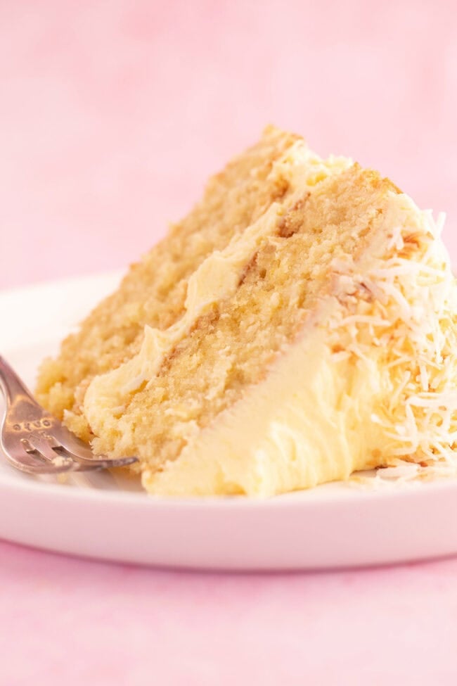 A beautiful slice of Lemon Coconut Cake on a pink backdrop.