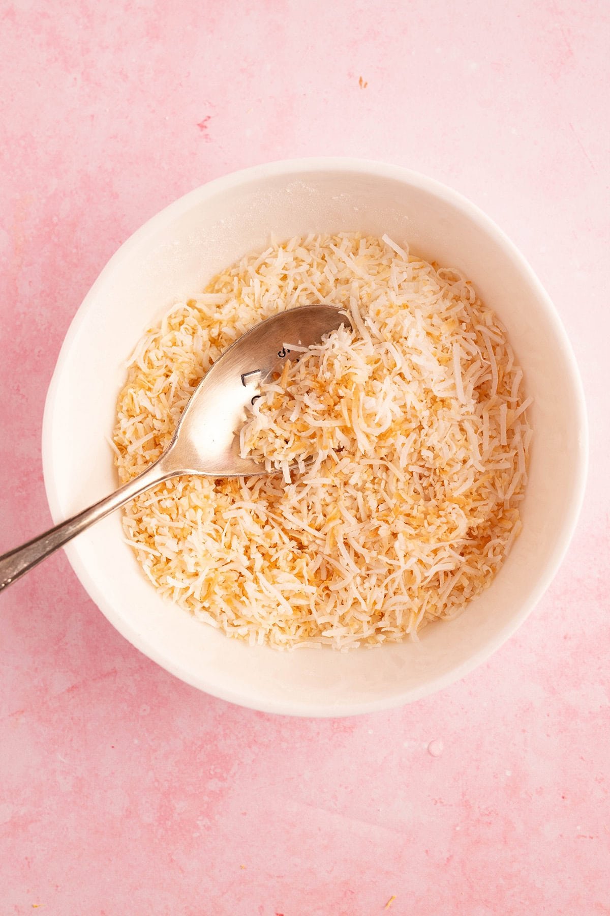 Top down view of a white bowl filled with toasted shredded coconut.