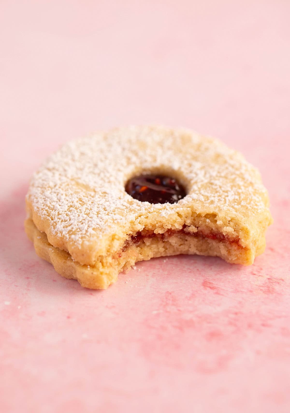 A close up of a homemade Linzer Cookie with a bite taken out of it.