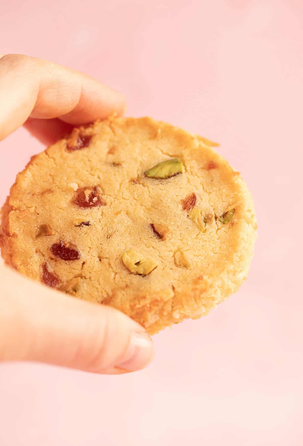 A hand holding a cookie on a pink backdrop. 