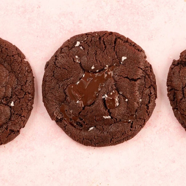 Three chocolate cookies on a pink backdrop.