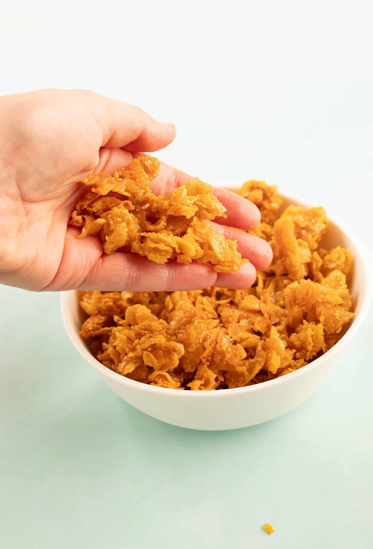 Jessica Holmes' hand reaching into a bowl of Cornflake Crunch.
