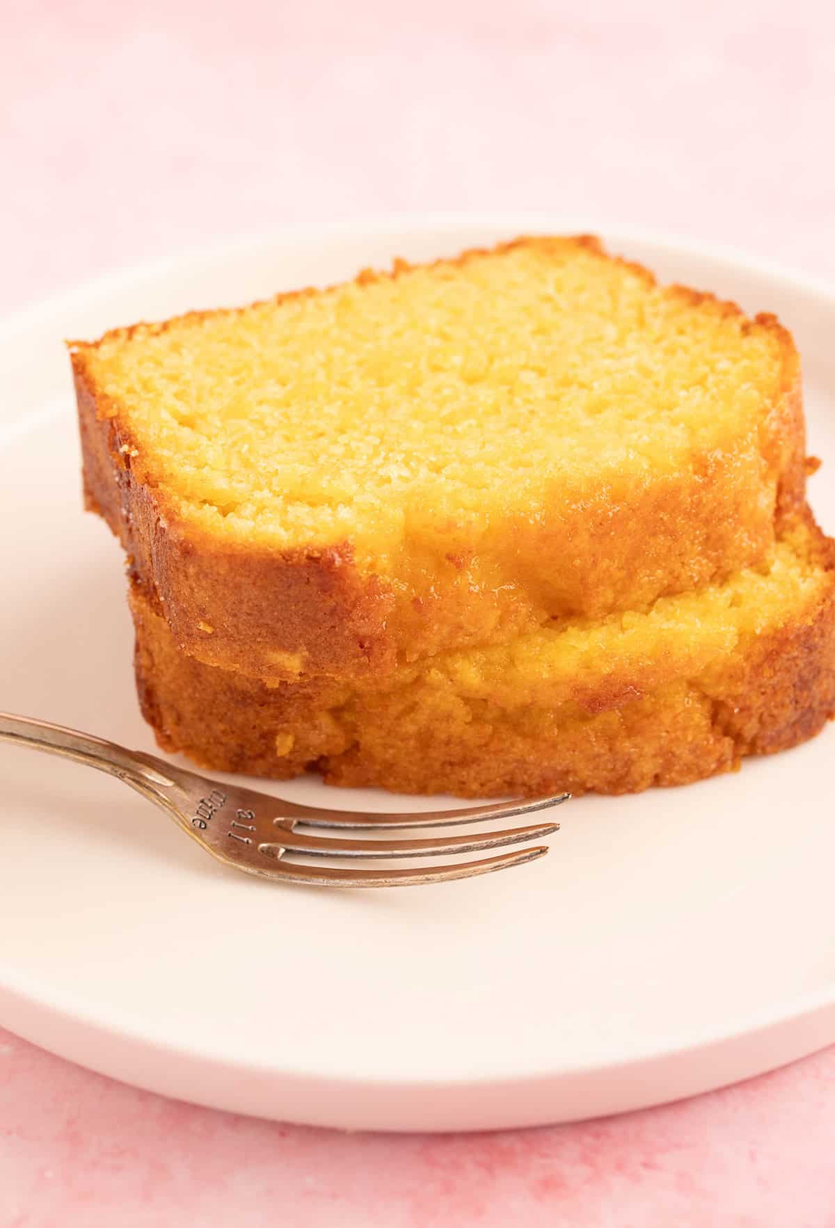 Two slices of orange cake on a white plate with a decorative fork.